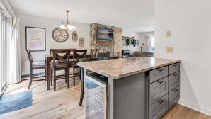 Une cuisine dotée d’un îlot central, d’un coin repas avec des chaises, d’une horloge et d’un mur d’accent en pierre.