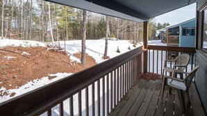 Eine Holzterrasse mit Geländer, einem Stuhl und Blick auf einen verschneiten Garten und Bäume.