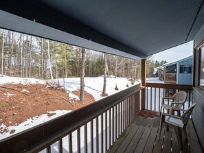 A wooden deck with a railing, a chair, and a view of a snow-covered yard and trees.