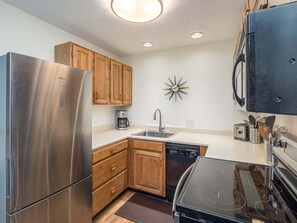 A kitchen with a stainless steel refrigerator, wooden cabinets, a dishwasher, an induction cooktop, and a microwave.