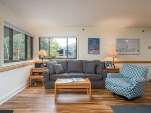 A living room with a grey sofa, a blue patterned chair, a wooden coffee table, and two side tables with lamps.