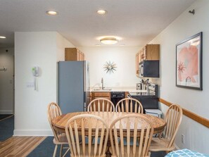 A compact kitchen with a dining area, wooden cabinets, a refrigerator, and a microwave.