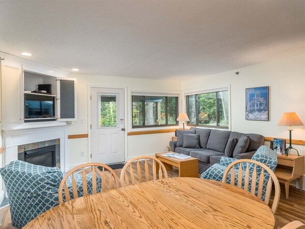 A cozy living room with a fireplace, a sofa, a dining table, and a TV mounted above the fireplace.