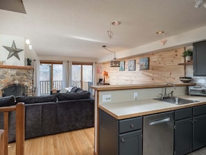 A modern kitchen with a stone fireplace, wooden accents, and a built-in island with a sink.