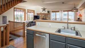 Una cocina con una escalera de madera, una chimenea de piedra y una isla grande con un fregadero.