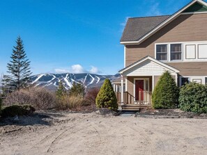 A two-story house with a front porch, a mountain backdrop, and a dirt driveway. - Powder Ridge Townhouse 41 (Newry)