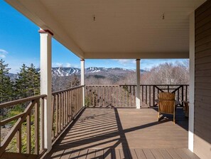 A wooden deck with a view of snow-capped mountains, a chair, and a railing.