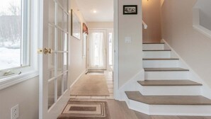 A hallway with a staircase, a door with glass panels, and a rug on the floor.