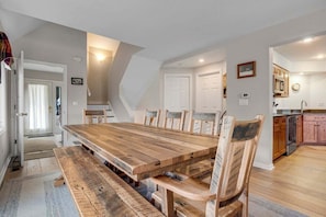 Zona pranzo con tavolo e sedie in legno, cucina sullo sfondo e una porta che conduce in un'altra stanza.