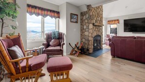 A living room with a stone fireplace, a television, and a view of the outdoors.