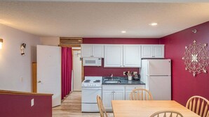 Une cuisine compacte avec des meubles blancs, un four à micro-ondes, une cuisinière et un réfrigérateur. On y trouve une table à manger avec quatre chaises.