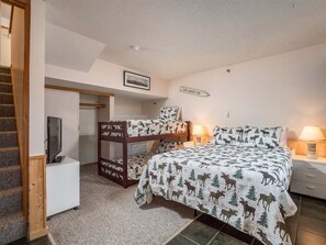 A bedroom with a bunk bed, a television on a stand, a bedside table with a lamp, and a framed picture on the wall. - Sunrise A-131 - Sunday River Condo (Newry)