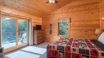 Une chambre dans une cabane en bois, avec un lit, une commode, un ventilateur de plafond et une porte-fenêtre coulissante donnant sur une terrasse extérieure.