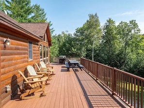 A wooden deck with Adirondack chairs, a grill, and a picnic table.