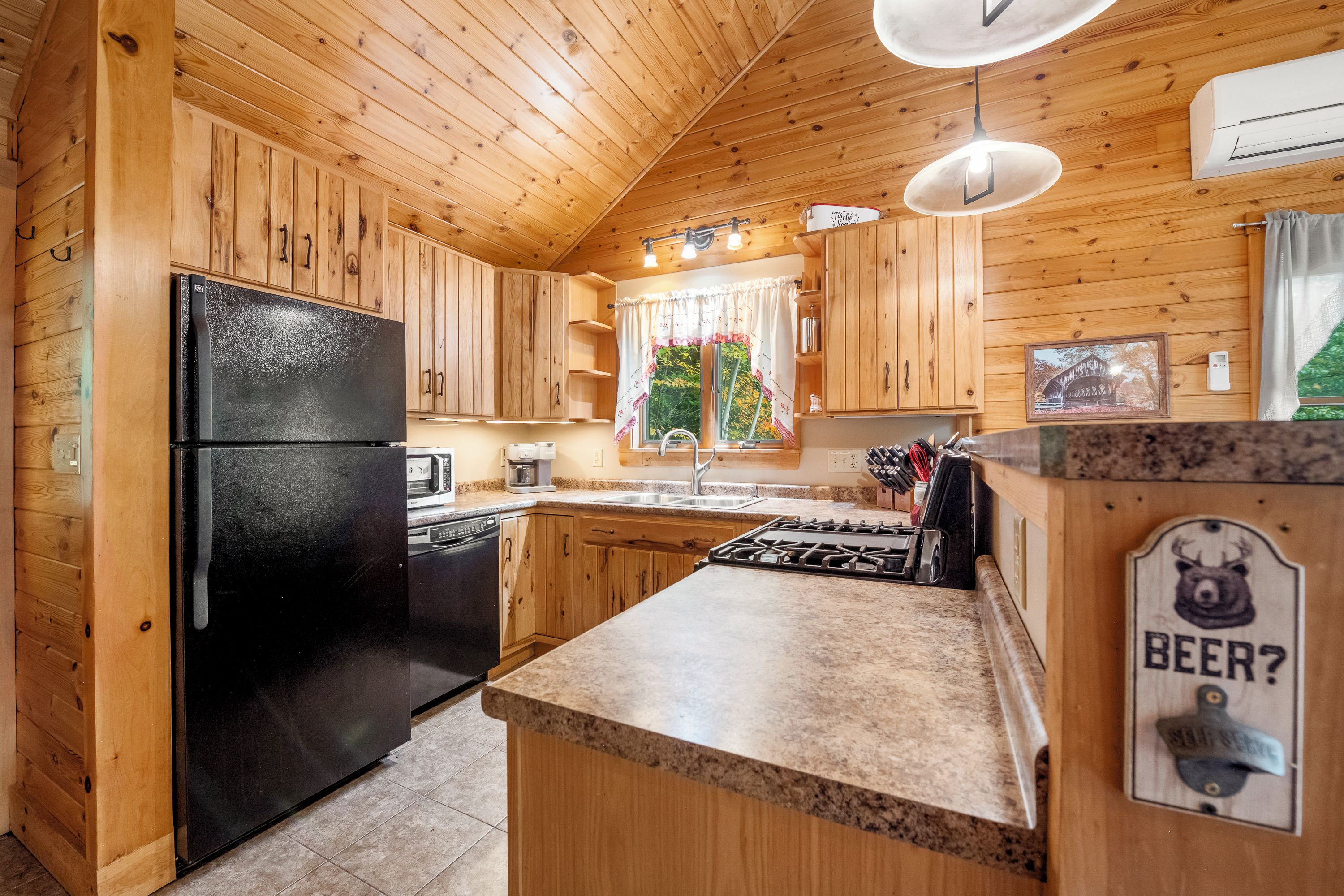 A wooden cabin kitchen with a black refrigerator, a stove, and a sink.