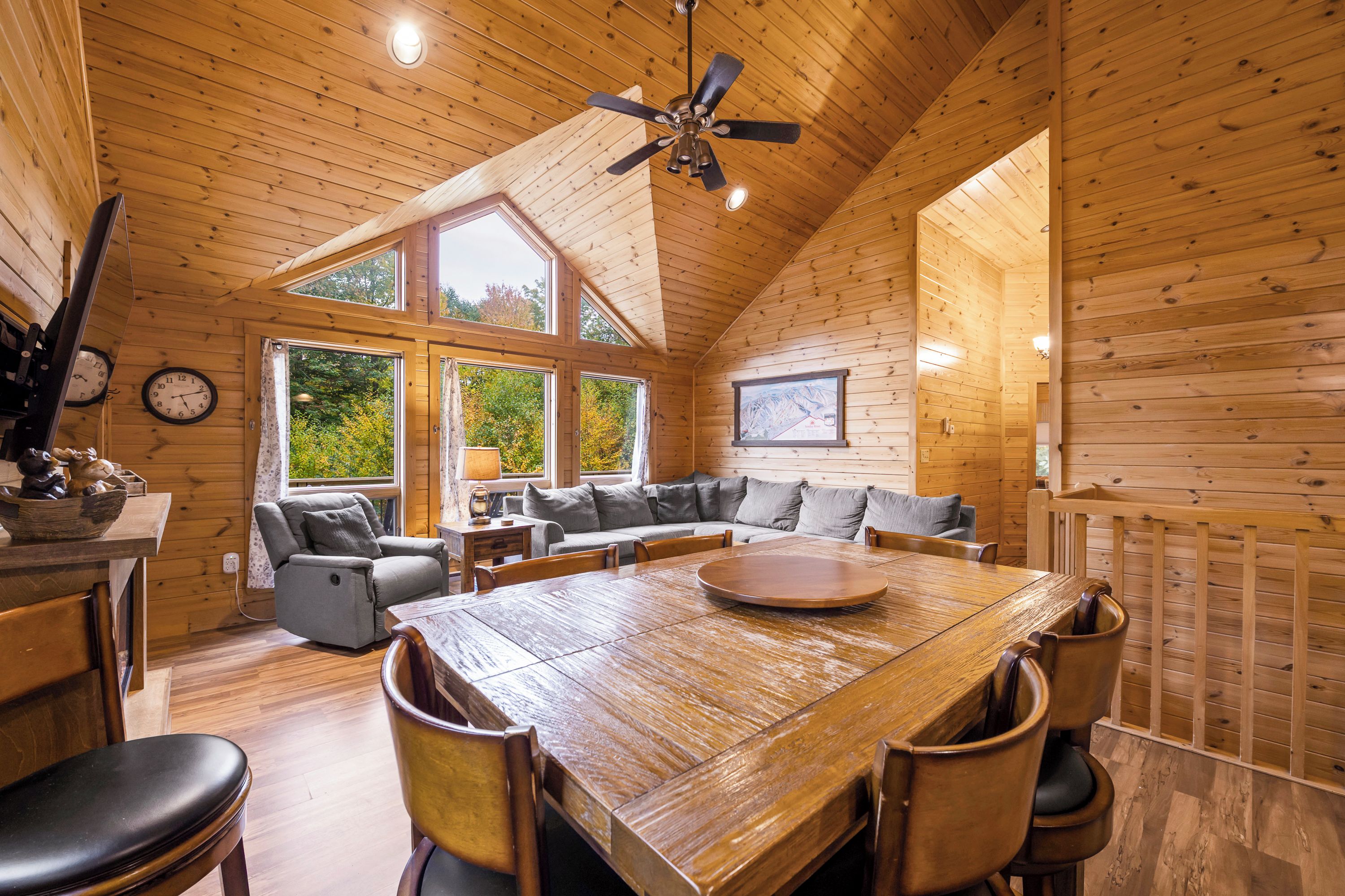 A log cabin interior with a dining area, seating, and a ceiling fan.