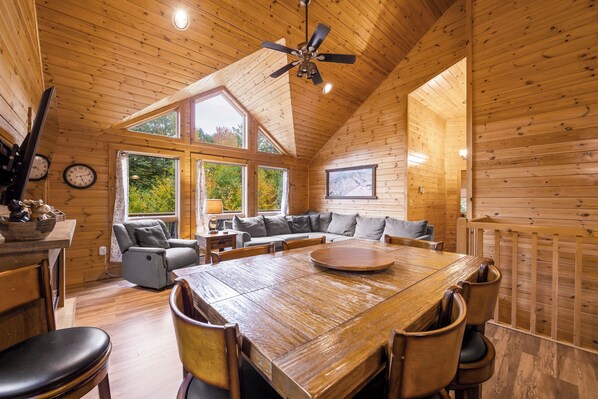 A log cabin interior with a dining area, seating, and a ceiling fan.