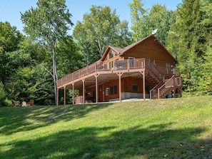 A wooden cabin with a balcony, a covered porch, and a staircase leading to the upper level.