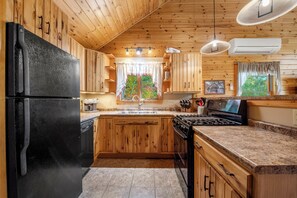 A kitchen with wooden cabinets, a black refrigerator, a stove, and a window with a view of trees.
