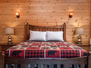 Une pièce aux murs lambrissés, comprenant un lit, deux lampes fixées au mur et une couvre-lit matelassée.
