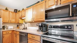 A kitchen with wooden cabinets, a stainless steel microwave, a coffee maker, and a dishwasher. - White Cap B-312 - Sunday River Condo (Newry)