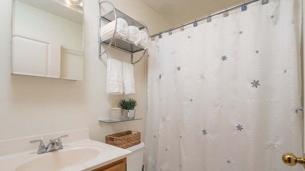 Un baño con un lavabo blanco, armarios de madera, un espejo, una cortina de ducha con motivos de estrellas y un inodoro.