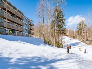Ein Skigebiet mit einem mehrstöckigen Gebäude, einer schneebedeckten Piste und Bäumen.