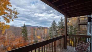 Una terraza de madera con vistas al follaje otoñal y montañas.