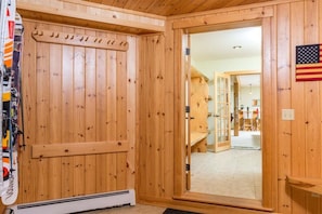 Une porte en bois avec un porte-skis, un drapeau américain et une vue sur une pièce où l’on aperçoit un banc et une table.