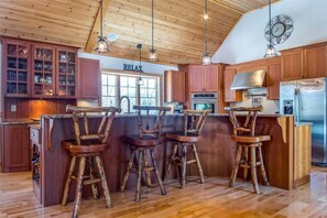 A kitchen with wooden cabinets, a bar area with stools, a stainless steel refrigerator, and a 'RELAX' sign on the wall. - Timberline Lodge at Sunday River (Newry)