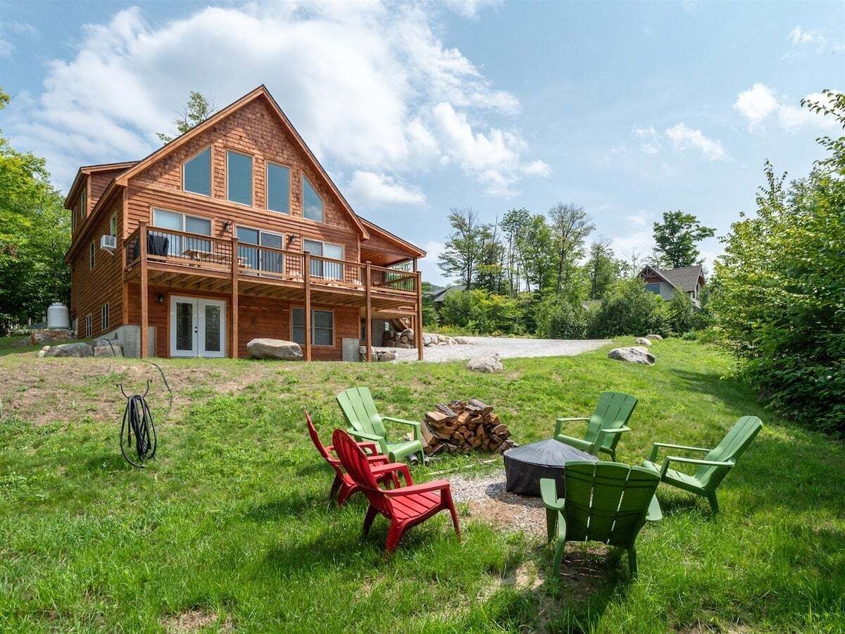Una cabaña de madera con terraza, rodeada de césped y mobiliario exterior.