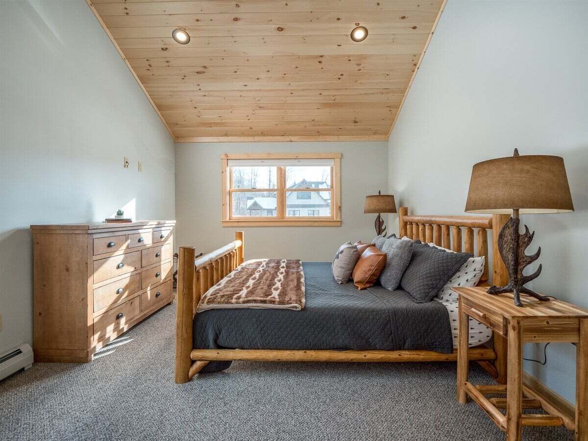 Ein Schlafzimmer mit einem hölzernen Bett, einem Schminktisch, einem Nachttisch, einer Lampe und einem Fenster.