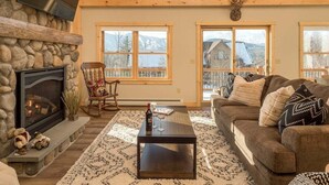 A cozy living room with a stone fireplace, a wooden ceiling, and large windows.