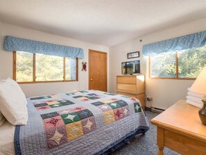 Un dormitorio con cama, cómoda, televisor y ventanas.