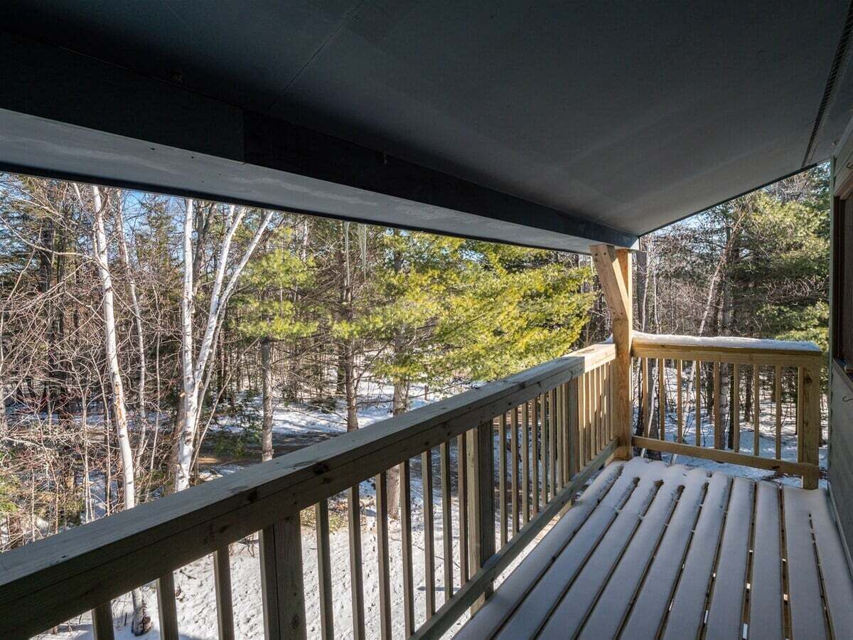 A wooden deck with a railing overlooking a snowy landscape with trees.