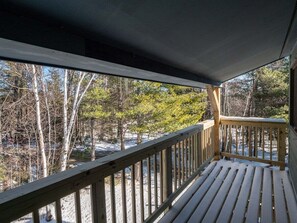 A wooden deck with a railing overlooking a snowy landscape with trees.
