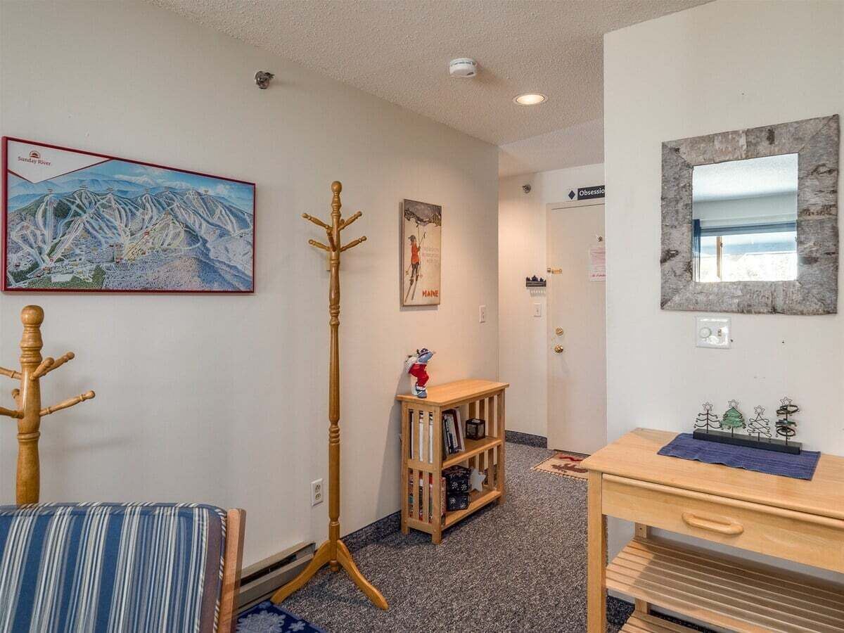 A room with a striped chair, a coat rack, a wooden bookshelf, a small table, and a painting on the wall.