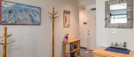 A room with a striped chair, a coat rack, a wooden bookshelf, a small table, and a painting on the wall.