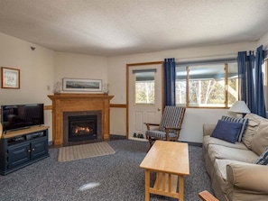 Una sala de estar con chimenea, televisor, sofá y ventana con cortinas.