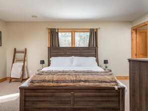 Un dormitorio con una cama de madera, una ventana con cortinas, una escalera y una mesita de noche con una lámpara.