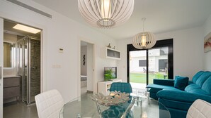 Een moderne woonkamer met een glazen tafel, een turquoise bank en witte stoelen.