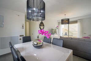 A modern living room with a dining table, chairs, a sofa, and a chandelier.