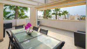 A glass-top table with chairs, a vase with flowers, and a view of palm trees and buildings. - Apartamento Vistabella (Vistabella Golf) (Orihuela Costa)