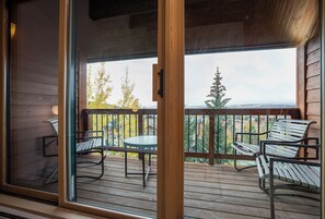 Enjoy a serene outdoor space with a round table and two chairs, surrounded by a railing and offering a scenic view of the surrounding landscape and distant mountains.