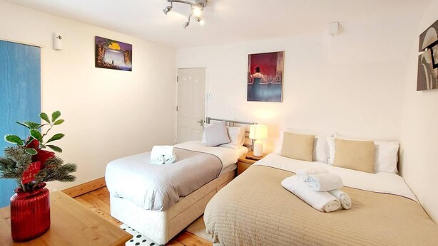A hotel room with two beds, a wooden floor, a red vase with a plant, and two wall-mounted lamps. - Beautiful 3-bed House in Chatham (Chatham)