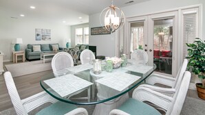 Un espace repas moderne avec une table en verre, des chaises en osier blanc et un luminaire suspendu.