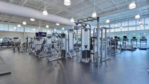 Une salle de sport spacieuse, dotée de divers appareils d’exercice, de grandes fenêtres et d’un plafond haut.