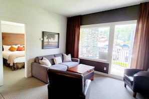 Une chambre d’hôtel moderne, équipée d’un lit, d’un canapé, d’une table basse et d’une grande fenêtre donnant sur l’extérieur.