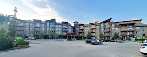 A multi-story hotel with a central entrance, multiple balconies, and a parking lot with several vehicles.