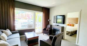A hotel room with a sofa, armchair, and a flat-screen TV mounted above a fireplace.
